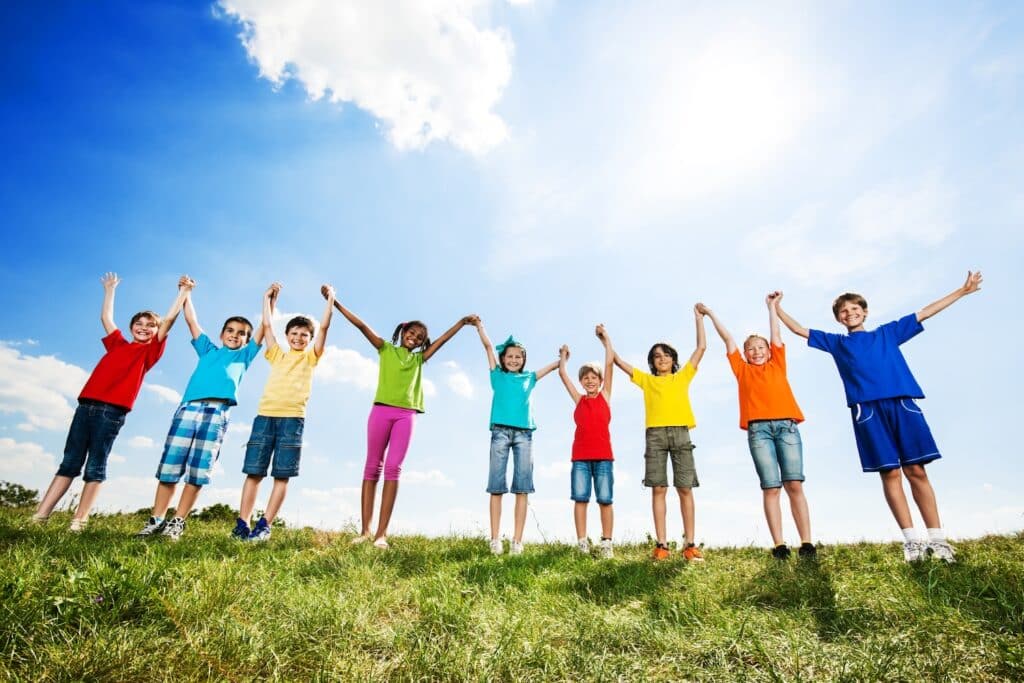 Large group of children with raised arms in nature.