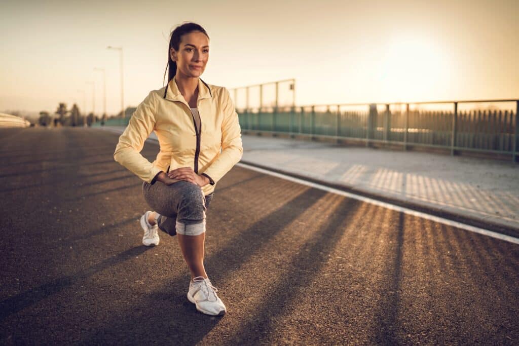 Smiling young woman doing stretching exercise at sunset.